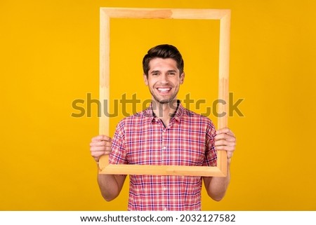 Photo of cheerful young happy man hold hands wooden frame smile picture isolated on yellow color background