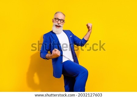 Photo portrait of bearded man in spectacles blue suit gesturing like winner isolated bright yellow color background Royalty-Free Stock Photo #2032127603
