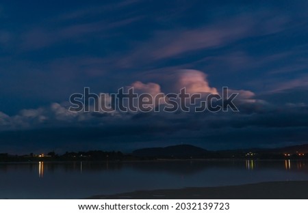dark ominous sky with light hitting a puff of white cloud and glowing pink in New Zealand.