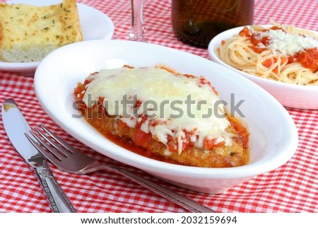 Chicken parmigiana with sides of spaghetti and garlic bread in individual plates. Royalty-Free Stock Photo #2032159694