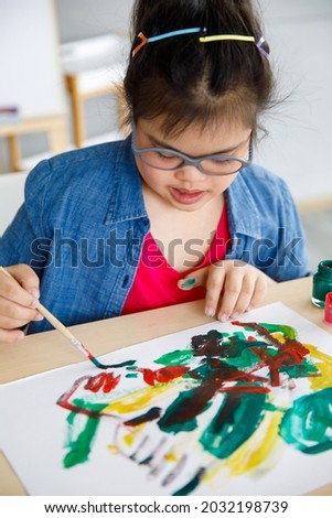High angle of creative Asian girl with Down syndrome painting abstract picture during art lesson. Special education for disable child.