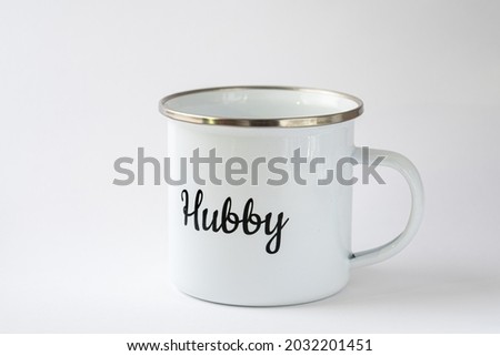 White enamel mug with a writing "Hubby" on it on a white background. Wedding accessories, cup for coffee or tea, luxury wedding. Royalty-Free Stock Photo #2032201451