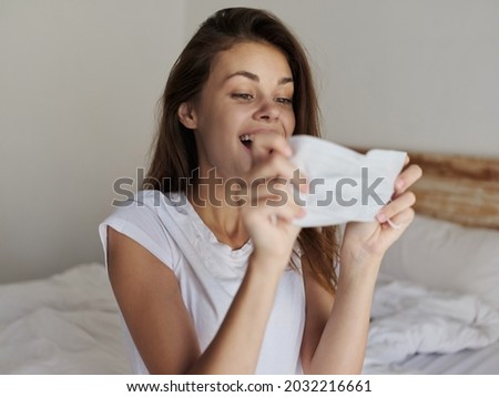 happy woman examines a medical mask in her hands and sits on the bed indoors
