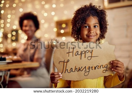 Happy black girl with Happy Thanksgiving sign at home with her mother in the background. 