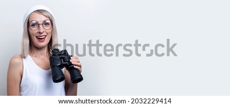 Cheerful young blonde woman with binoculars on a light background. Banner.