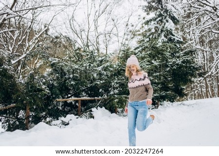 Happy woman in a pink coat and hat running on a winter trail in the park. Leisure concept, winter time.
