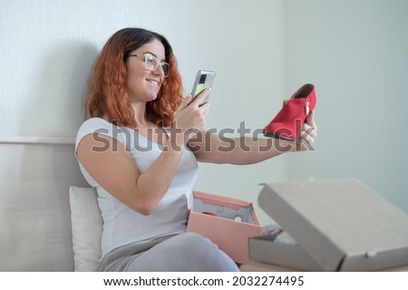The woman unpacks the delivered shoes. The girl leaves a review about the order in the application on the smartphone