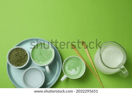 Cup of matcha latte and accessories for making on green background