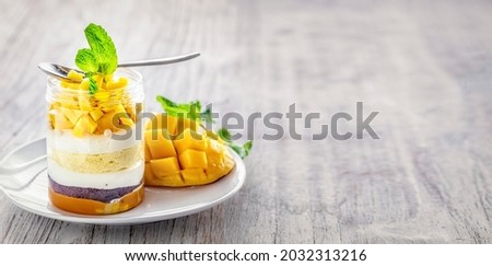 Homemade Mango dessert, cheesecake, trifle, mouse in a glass jar with spoon on a light grey wooden background, with copy space  Royalty-Free Stock Photo #2032313216