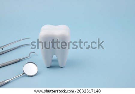 Healthy tooth model with stainless steel dental tools set on blue background. Royalty-Free Stock Photo #2032317140