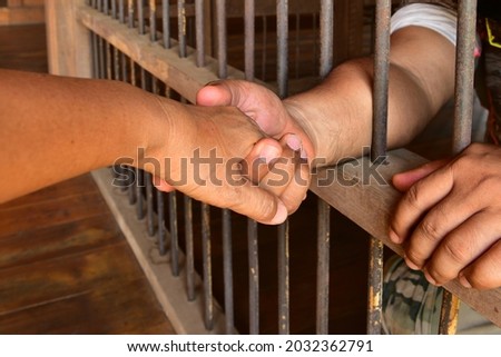 Holding hands and caring through the prison room wall. Royalty-Free Stock Photo #2032362791