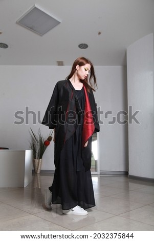 Full length image of young European lady wearing dramatic outfit composed of long black dress and a loose robe. Catalog shooting for online store or magazine. Studio editorial photography, copy space
