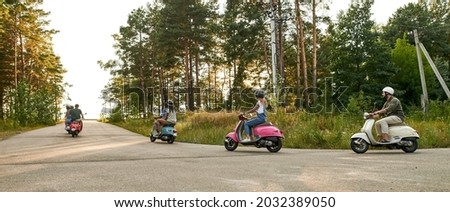 Young multiracial company riding scooter motorbikes along asphalt road in sunny nature, panorama. Leisure, fun and entertainment concept