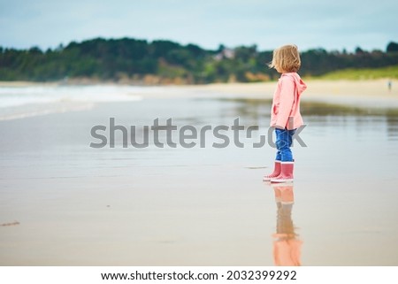 Adorable toddler girl on the sand beach at Atlantic coast of Brittany, France. Small child enjoying vacation by the sea or ocean. Travelling with kids