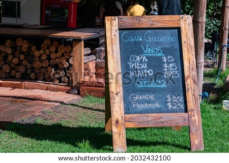chalk blackboard written with the menu of some restaurant.  In the background you can see woods and people cooking