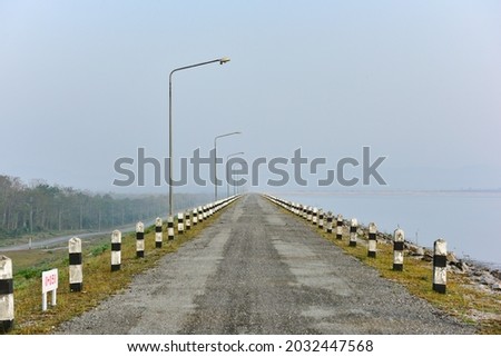 The road on the ridge of the dam in the countryside is straight in the morning mist.
