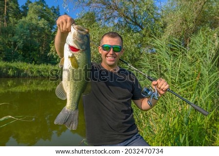 Bass fishing. Big bass fish in hands of pleased fisherman. Largemouth perch at pond Royalty-Free Stock Photo #2032470734
