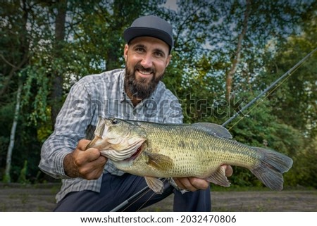 Bass fishing. Happy fisherman with big bass fish. Largemouth perch at pond Royalty-Free Stock Photo #2032470806