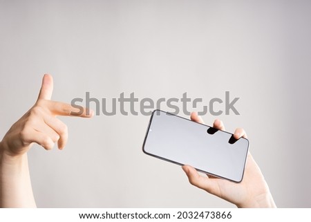 Look at the screen, point your finger at the smartphone screen, horizontally, panoramic photo or video. Phone in women's hands. Layout for design, mockup, light grey background