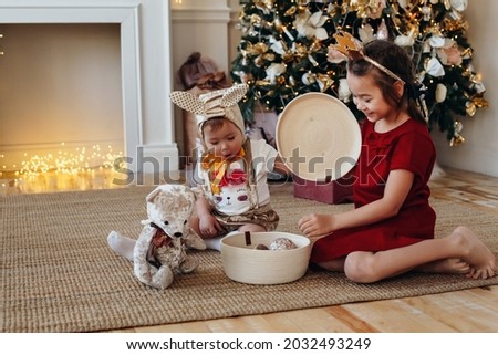 two sisters are playing with gifts and toys against the background of a Christmas fireplace and a tree. new year and christmas concept. A beautiful photo of children-girls in the New Year's interior. 