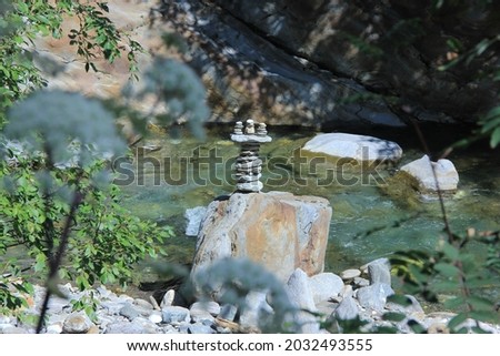 Artful stone heap with three tops, standing at the side of a river to indicate the way, surrounded by blurry foliage, alps stone heap way points