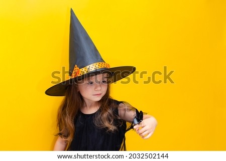 Halloween. A girl in a witch costume holds a black butterfly on her hand. Magic and mysticism. Yellow background, space for text. High quality photo