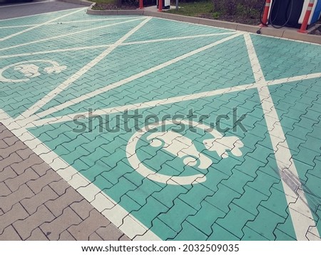 Electric car parking spot with charger. Green parking spot, electric car sign. Green paving stones. Car charging concept.   