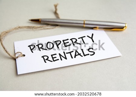 white card with text PROPERTY RENTALS with metal pen on gray background