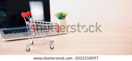 Close up the mini shopping cart and laptop at desk concept using the internet application for online shopping buying and spending on computer technology.