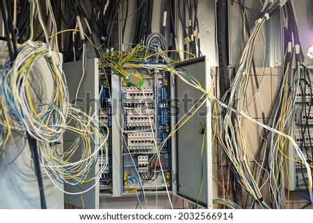 Tangled wires in electrical cabinet. Electric and mains wires are tangled. Concept - adjustment of power grid. open electrical cabinet with tangled wires. Electrification adjustment. Royalty-Free Stock Photo #2032566914