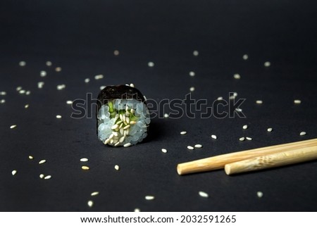 Roll with cucumber on a black background sesame seeds next to sushi chopsticks close-up shot