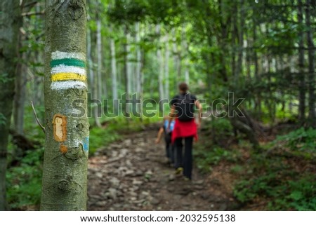 Green, yellow marking of the hiking trail, painted on a tree. Marking will lead us to our destination without wandering along the way. Wandering tourists in the background.