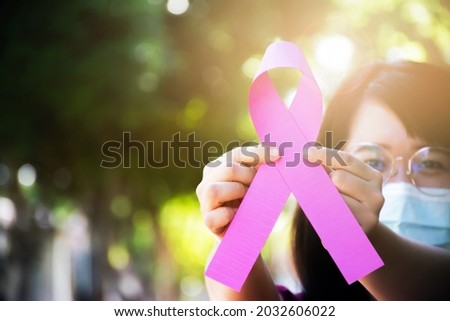 Pink paper ribbon in hand of Asian woman with blurred background , concept for supporting woman who has gotten breast cancer around the world.
