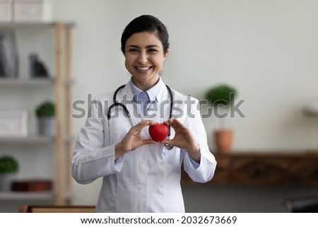 Happy confident indian ethnicity female young doctor cardiologist holding heart figure in hands, reminding regular checkup procedures for patients, promoting charity donation or healthcare services. Royalty-Free Stock Photo #2032673669
