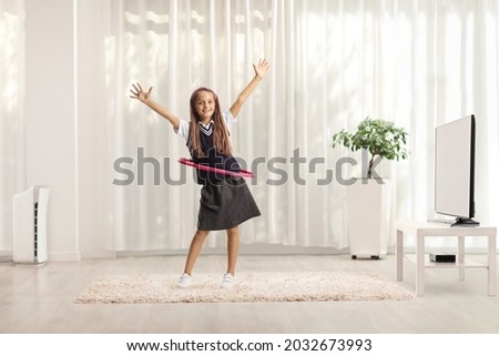Playful schoolgirl dancing with a hula hoop at home in a living room