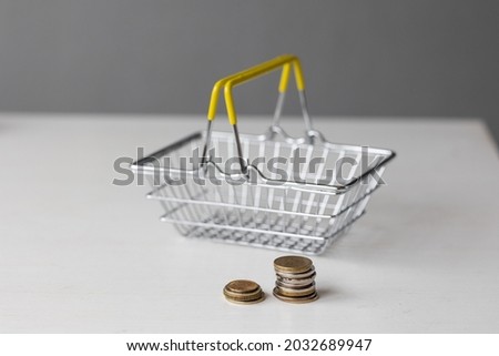 an empty metal supermarket food basket with coins on a white table with paper money, a woman's hand holding a dollar, calculating the cost of food and money costs, prices for finished products and