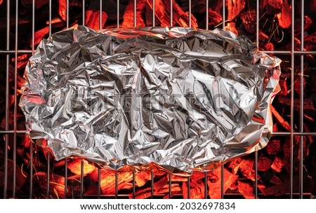 Some food in aluminum foil on  grate over hot pieces of coals. Top view.