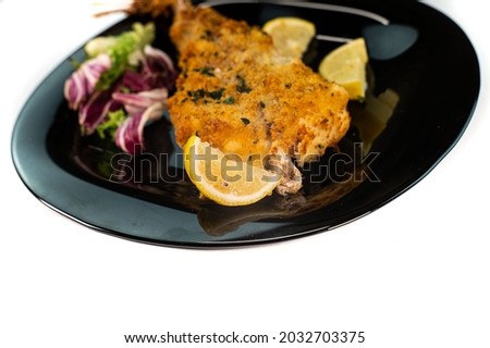 black plate with breaded monkfish on white background