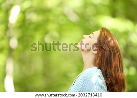 Side view portrait of a redhead woman breathing fresh air in a forest Royalty-Free Stock Photo #2032713410