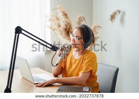 Cheerful woman host streaming his podcast using voice microphone. Female podcaster making audio stream in her small studio