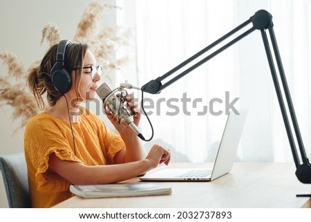 Female podcaster recording her podcast using microphone and laptop at his home broadcast studio. Woman streaming live from homemade radio studio