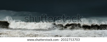 Panoramic view of a stormy sea and dark cloudy sky, big waves are crashing on the shore