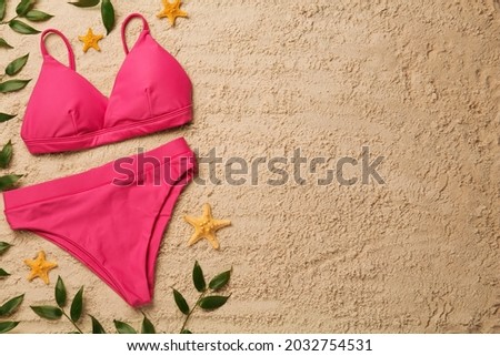 Stylish bikini, starfishes and green leaves on sand, flat lay. Space for text