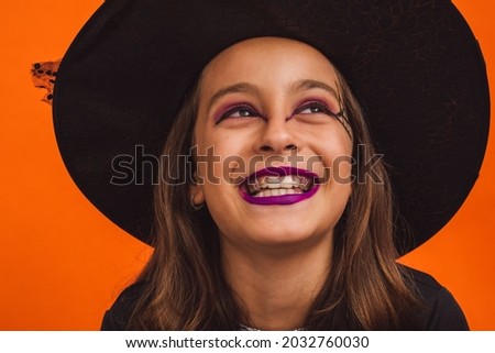 Portrait of a very smiling little witch against an orange background on Halloween