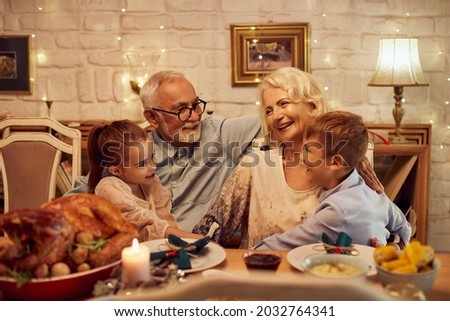 Happy grandparents talking to their grandchildren during Thanksgiving meal at dining table at home. Royalty-Free Stock Photo #2032764341