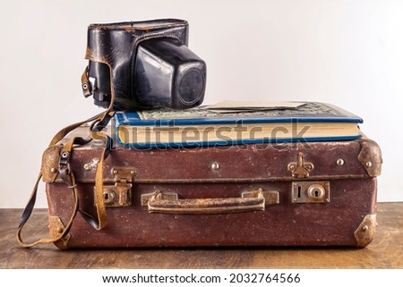 An old vintage brown suitcase with a retro camera in a leather case, an album with photos on a wooden table