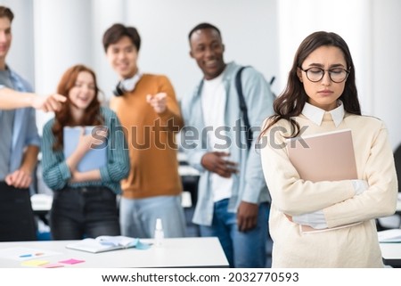 Group Conflict. Sad latin woman in eyeglasses standing away alone, suffering humiliation and public disgrace, crowd of bad people bullying pointing fingers at victim, laughing. Discrimination, Gossip Royalty-Free Stock Photo #2032770593