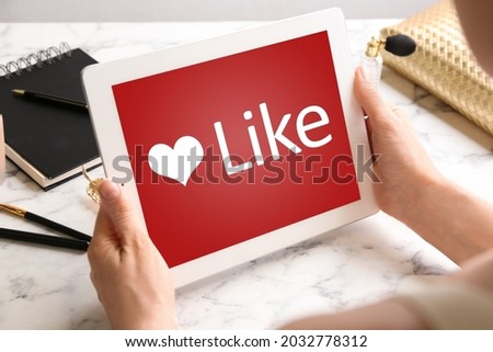 Woman using tablet with word Like on screen at table, closeup