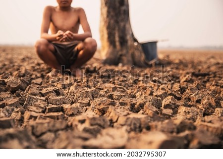 Sad a boy sitting on dry ground .Seedling wither on dry land. As the young man's hand was gently encircled. concept hope and drought Royalty-Free Stock Photo #2032795307