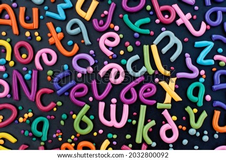The letters of the English alphabet made of plasticine of different colors are laid out in a chaotic order on a black background Royalty-Free Stock Photo #2032800092